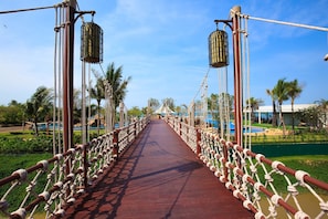 A rope bridge with a red walkway, surrounded by greenery and palm trees. - Mövenpick Siam Hotel Na Jomtien Pattaya (Sattahip)