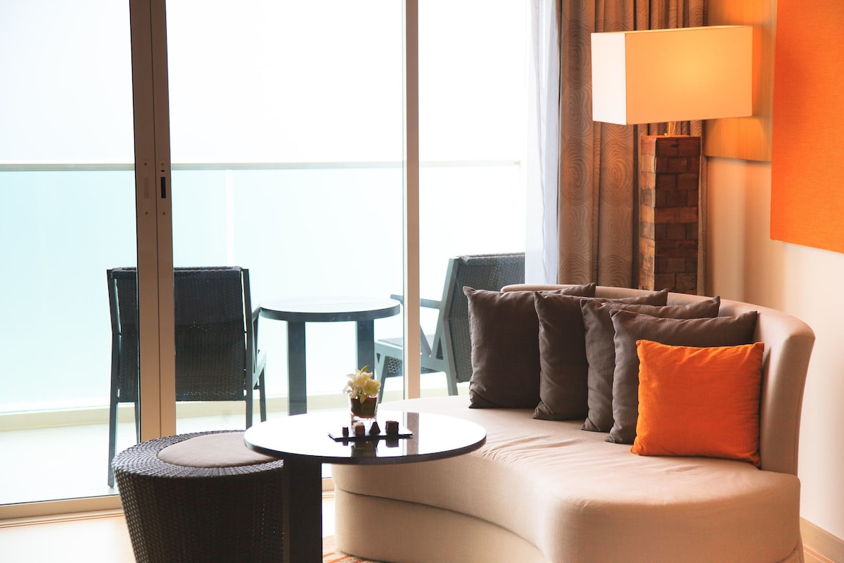 A modern hotel room with a curved sofa, a small round table, and a view of the balcony.
