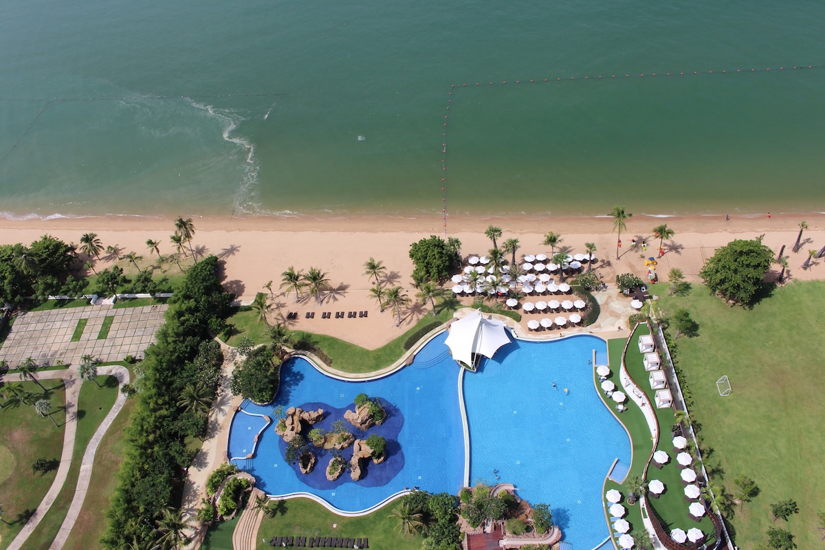 An aerial view of a resort with a swimming pool, beach, and palm trees.