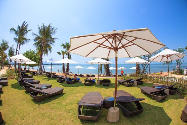 A beachside lounge area with wicker loungers and umbrellas, overlooking the ocean.