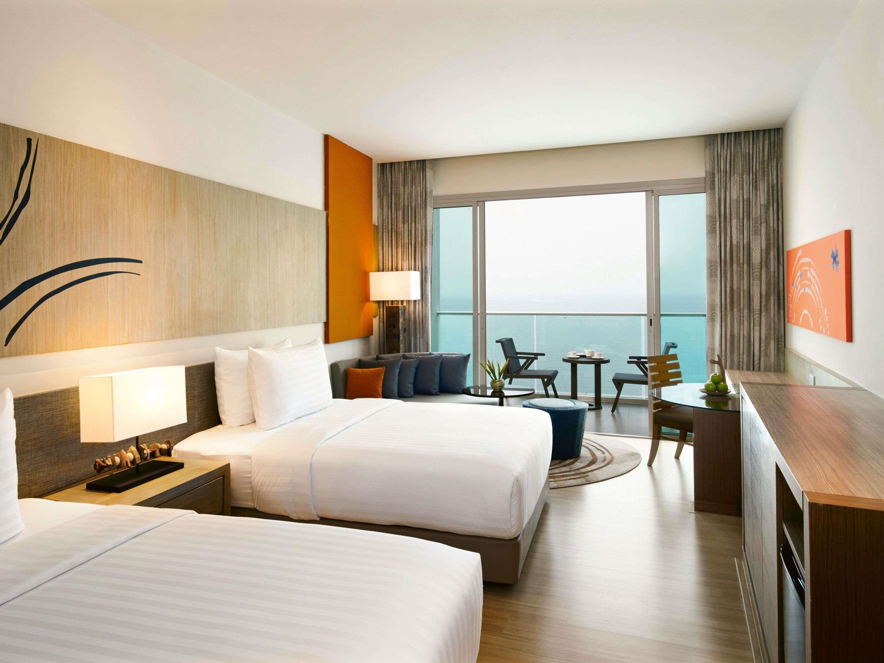 Ein Hotelzimmer mit zwei Betten, einem Schreibtisch, einem Stuhl, einem kleinen Tisch und Meerblick.