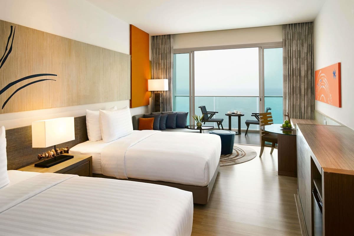 Une chambre d’hôtel avec deux lits, un bureau, une chaise, une petite table et une vue sur la mer.