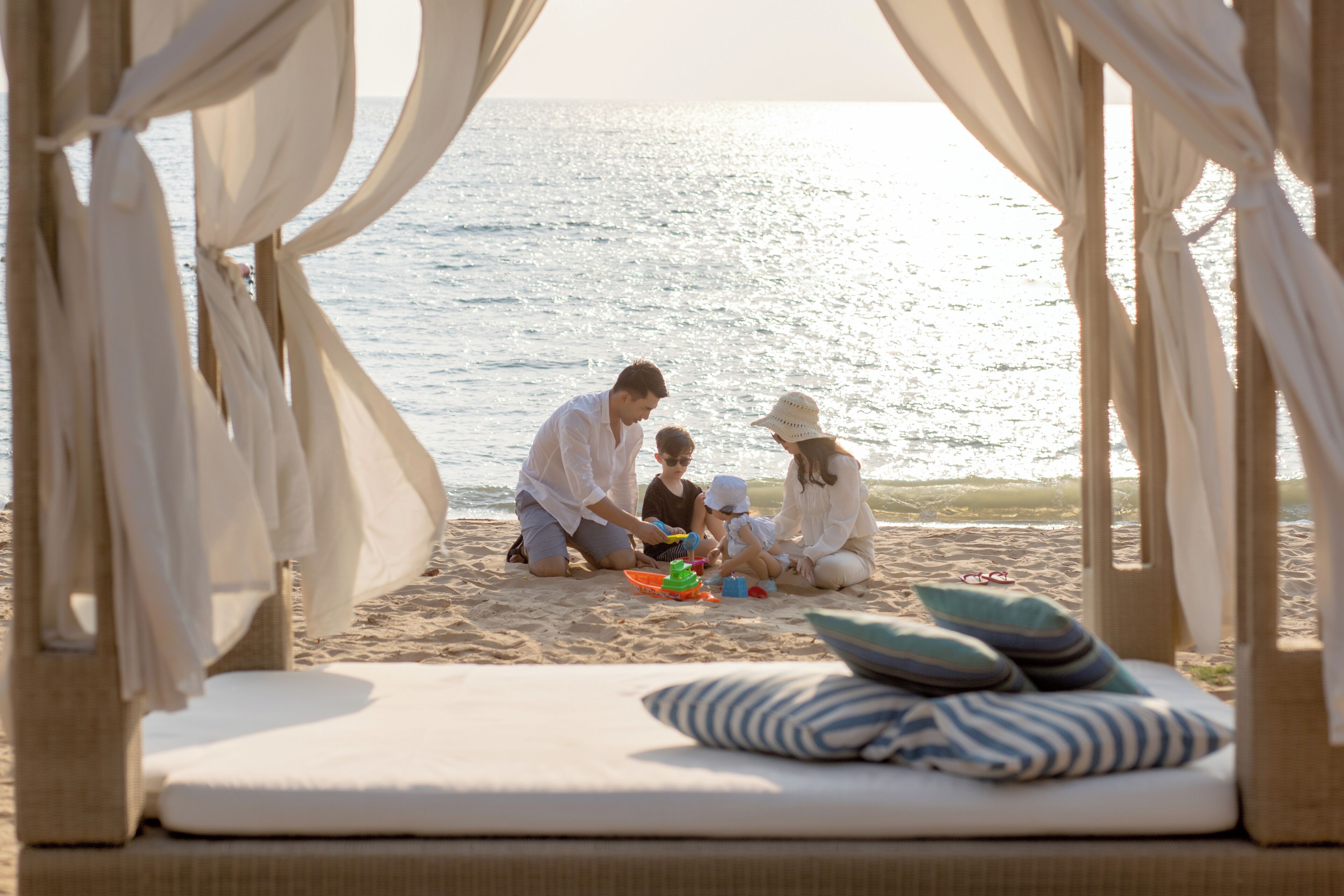 A beach setting with a family playing on the sand, a beach chair with pillows, and a view of the sea.