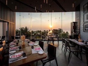 En restaurant med udsigt til solnedgang, store vinduer og et moderne interiør.