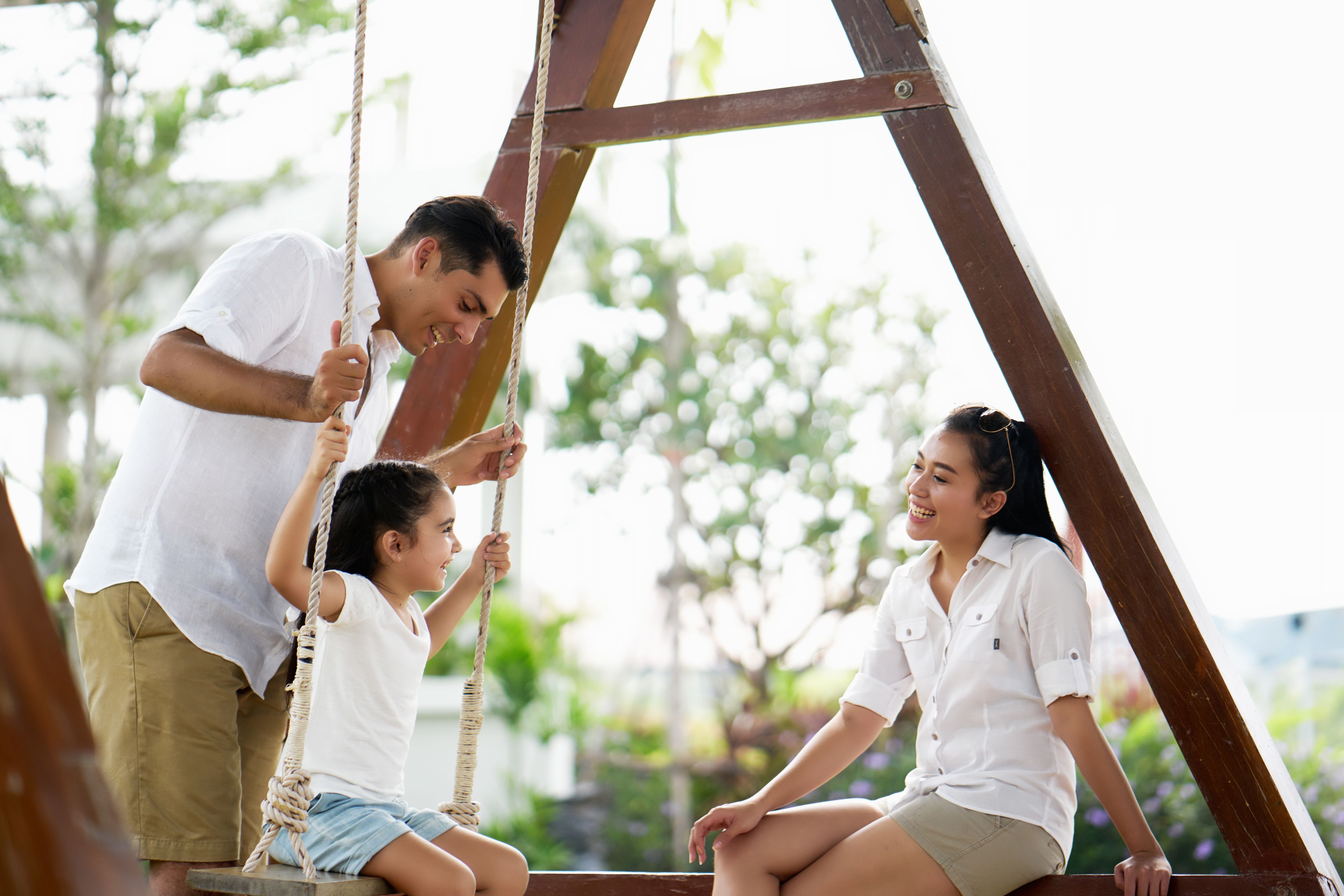 A wooden swing set in an outdoor setting with greenery in the background.