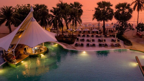A resort pool with lounge chairs and umbrellas, palm trees, and a sunset view. - Mövenpick Siam Hotel Na Jomtien Pattaya (Sattahip)