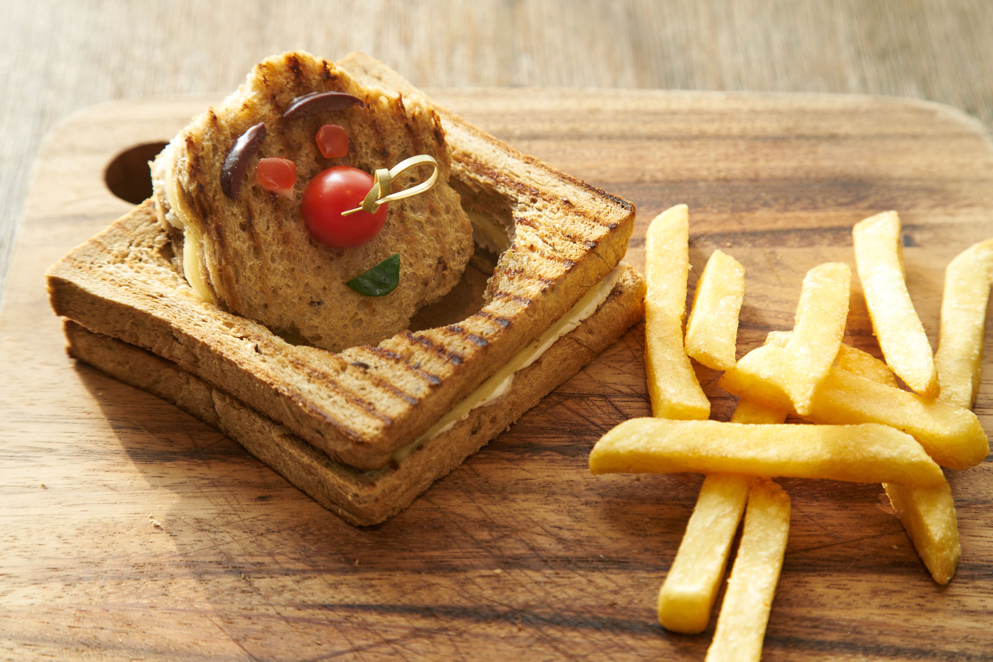 Sanduíche sobre tábua de madeira com batatas fritas ao lado.