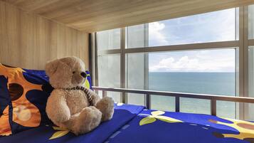 Een kamer met een groot raam, een bed met een deken met blauw en geel dessin, en een teddybeer op het bed.