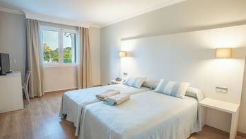 A hotel room with two beds, a desk, a chair, a TV, and a window with curtains.