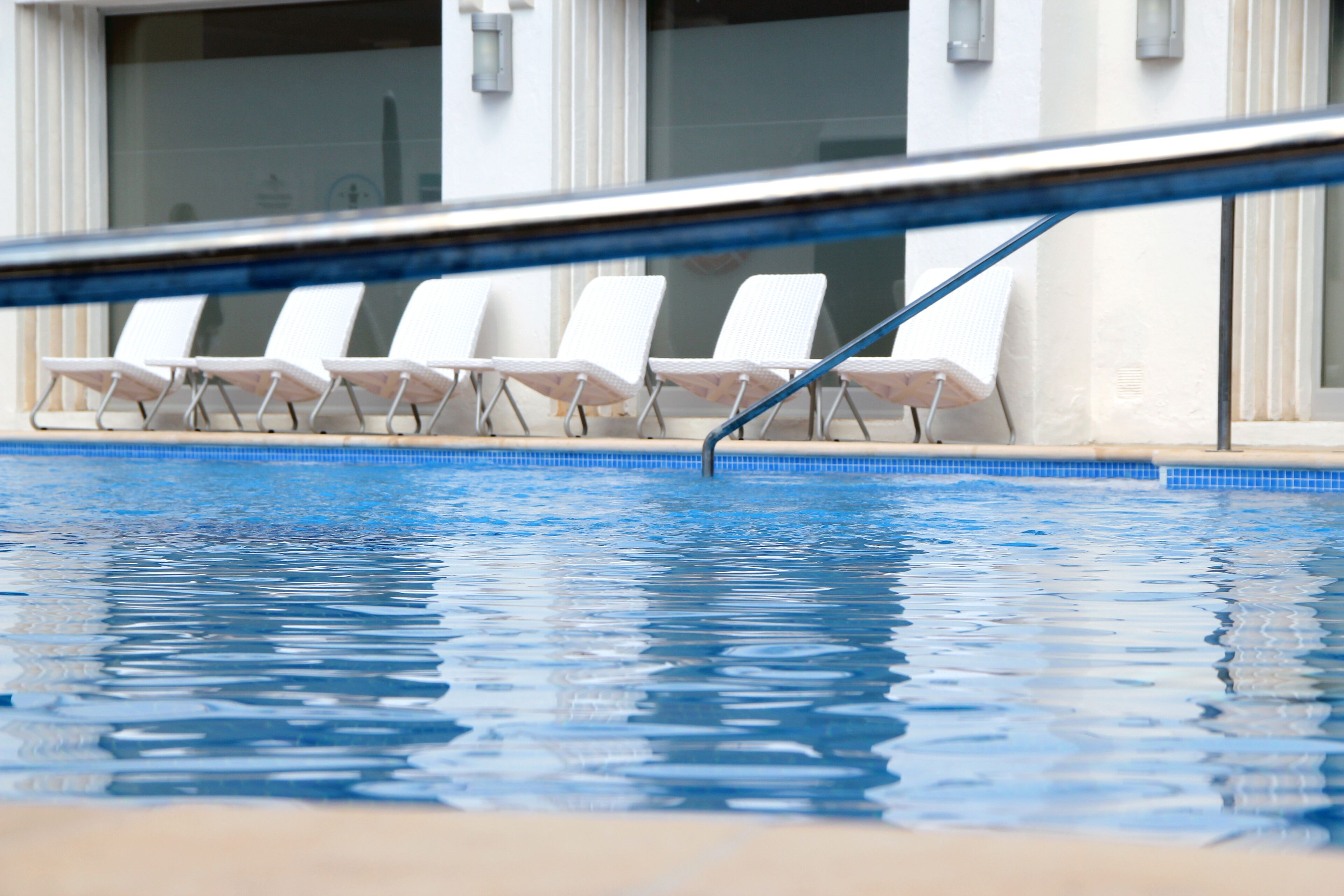 A swimming pool with white lounge chairs and a blue tiled edge.