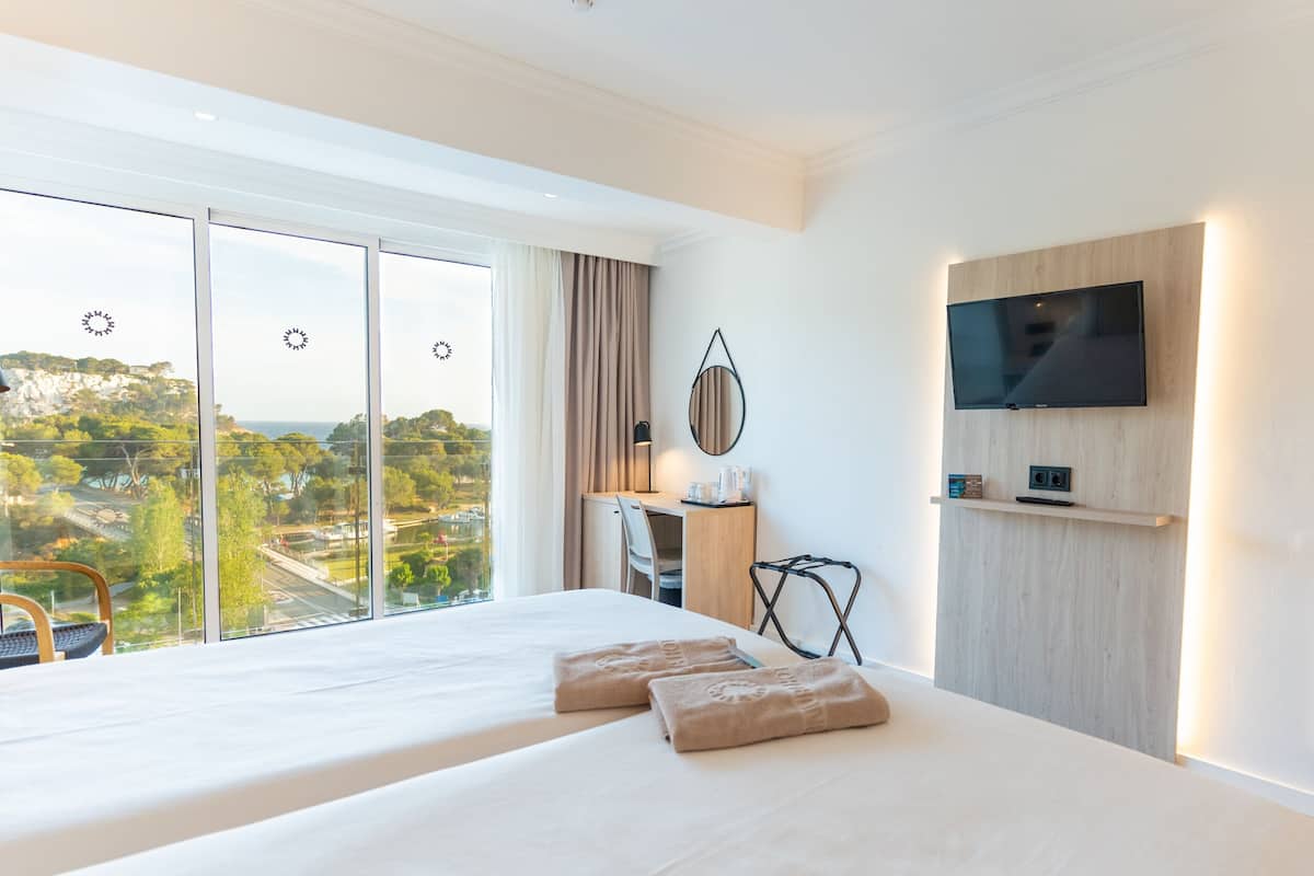 A hotel room with a large bed, a desk, a chair, a TV mounted on the wall, and a view of the outdoors.