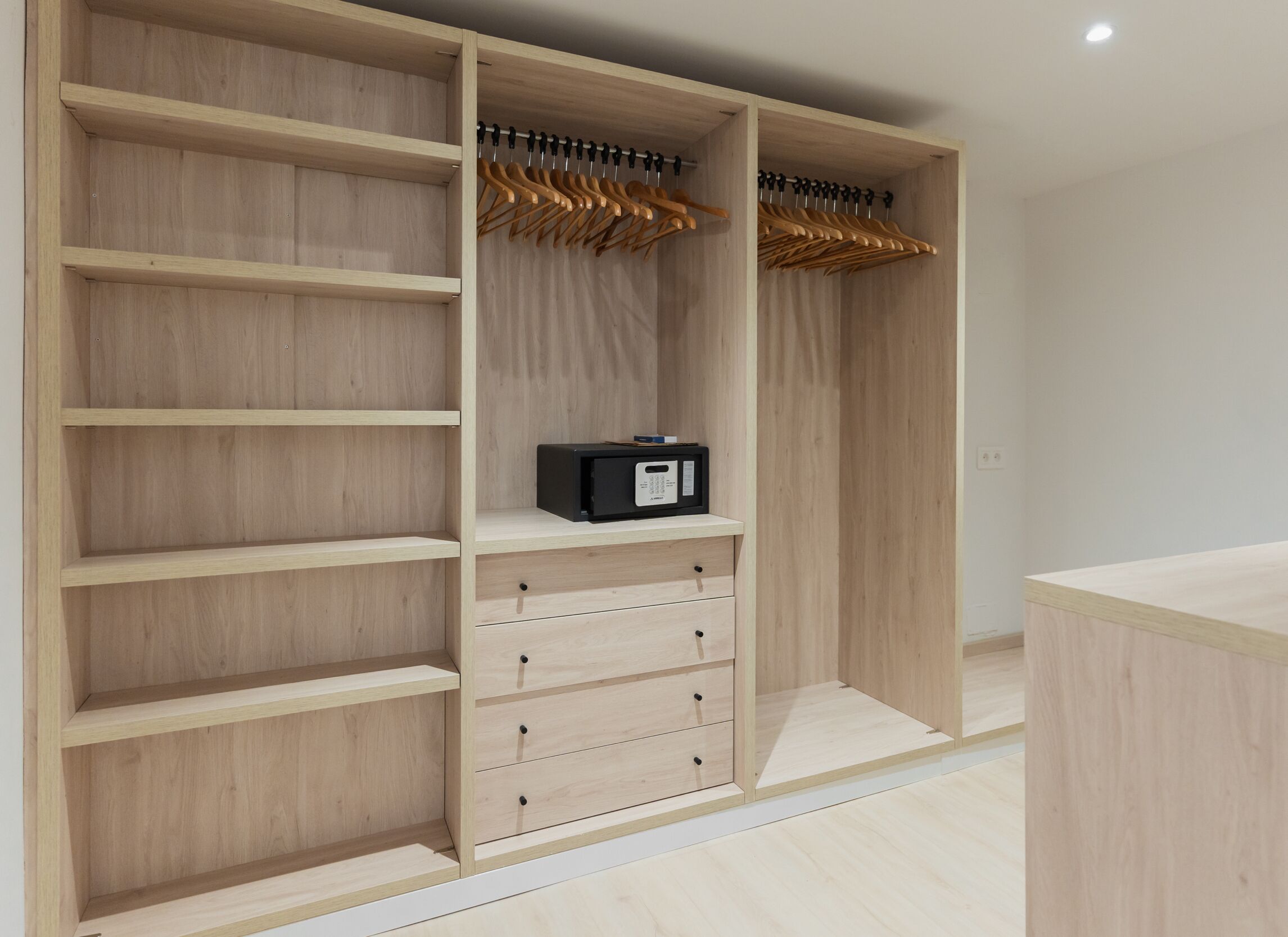 Een houten garderobe met meerdere planken en lades, een kledingstang, en een klein zwart elektronisch apparaat op een van de planken.