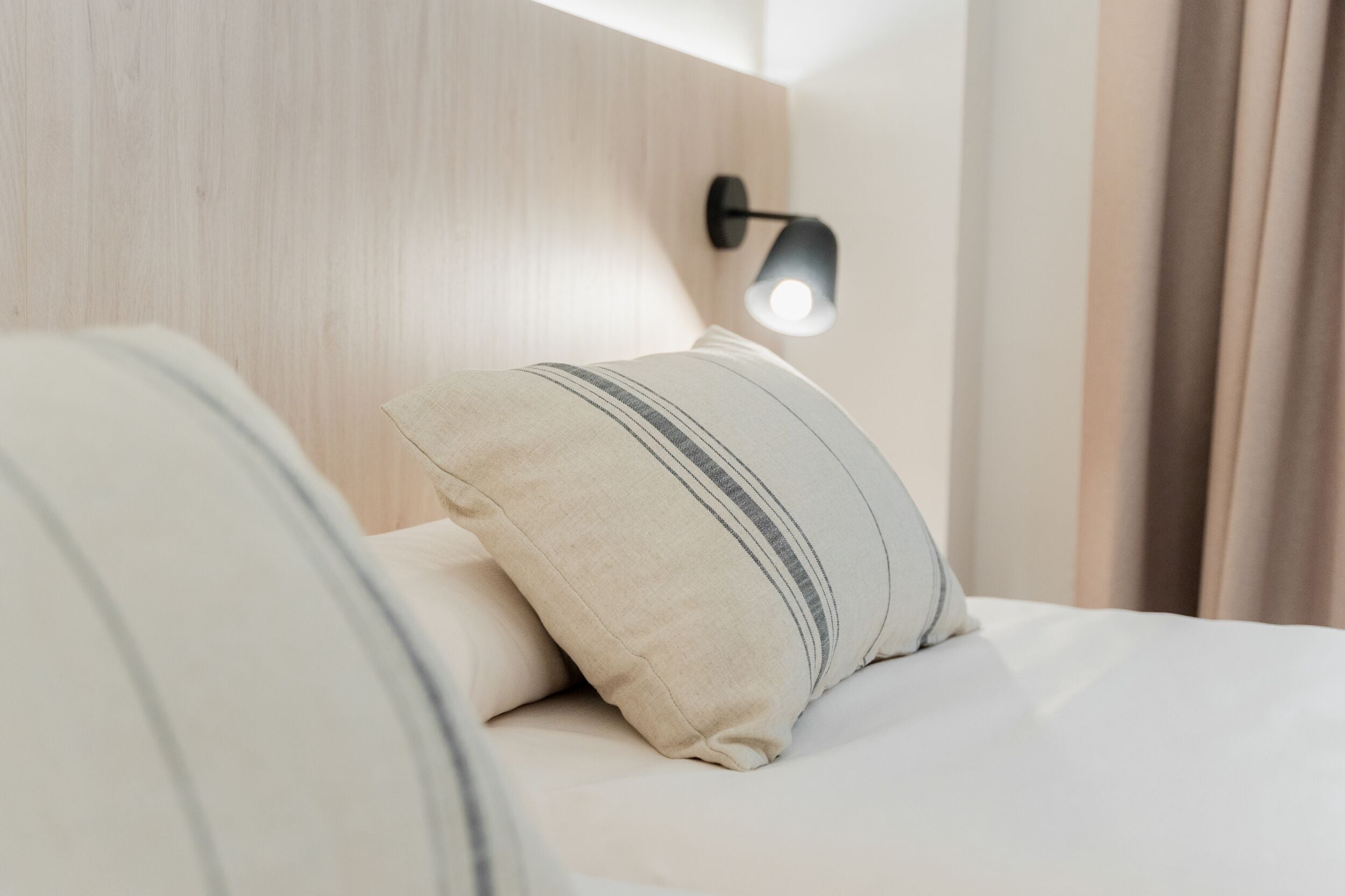 Un lit bien fait, avec un oreiller à rayures et une lampe fixée au mur.
