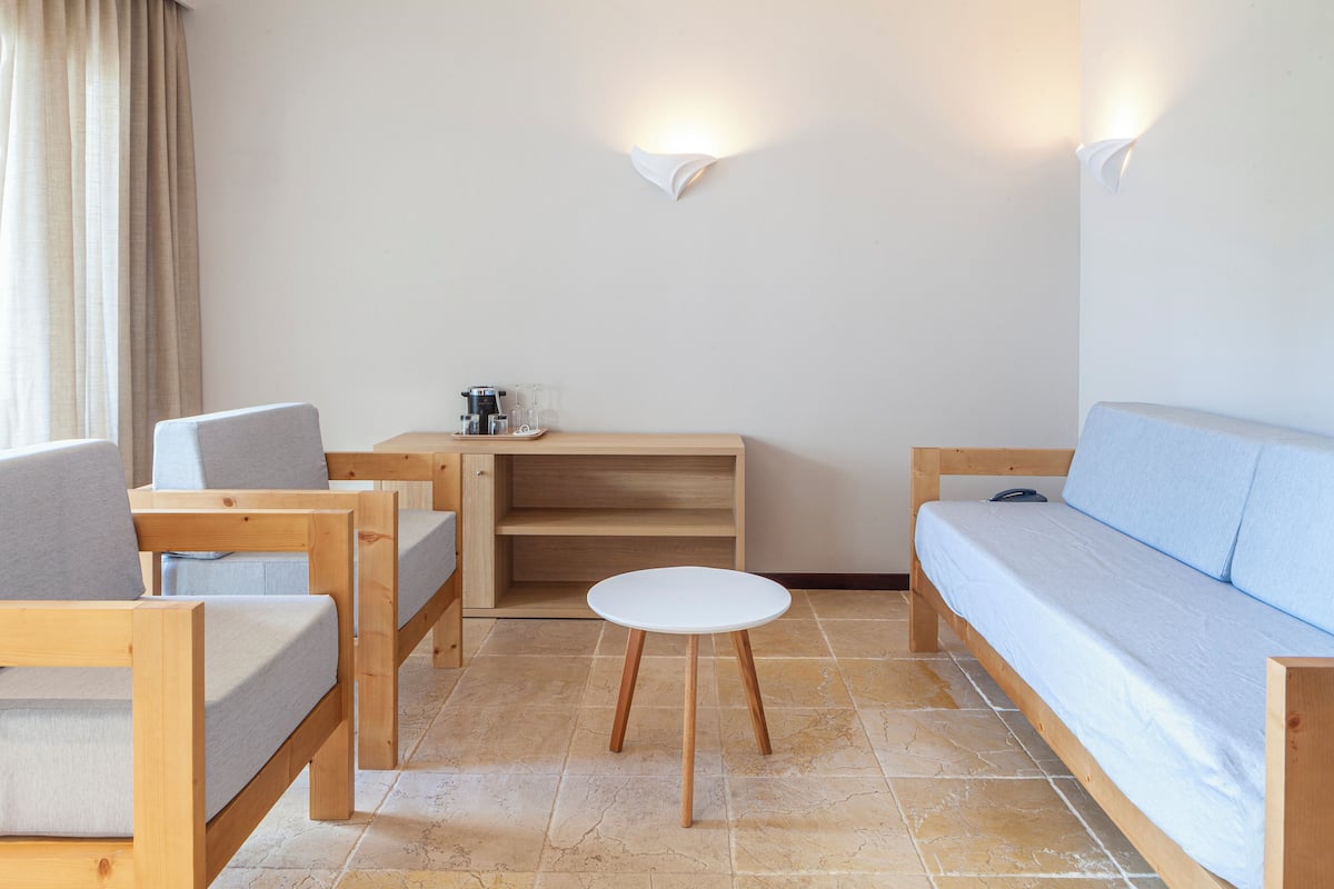 A room with a wooden sofa, two armchairs, a small round table, and a wooden cabinet.