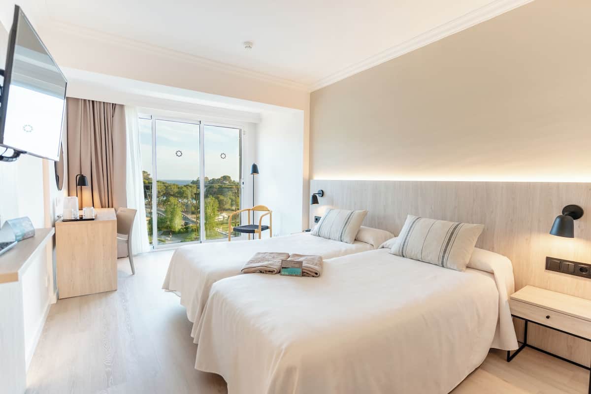 A hotel room with two beds, a desk, a chair, a TV, and a balcony with a view.