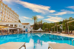 A swimming pool with lounge chairs and umbrellas, surrounded by a building with multiple floors and balconies. - Minura Hotel Cala Galdana & Apartamentos (Ciutadella de Menorca)