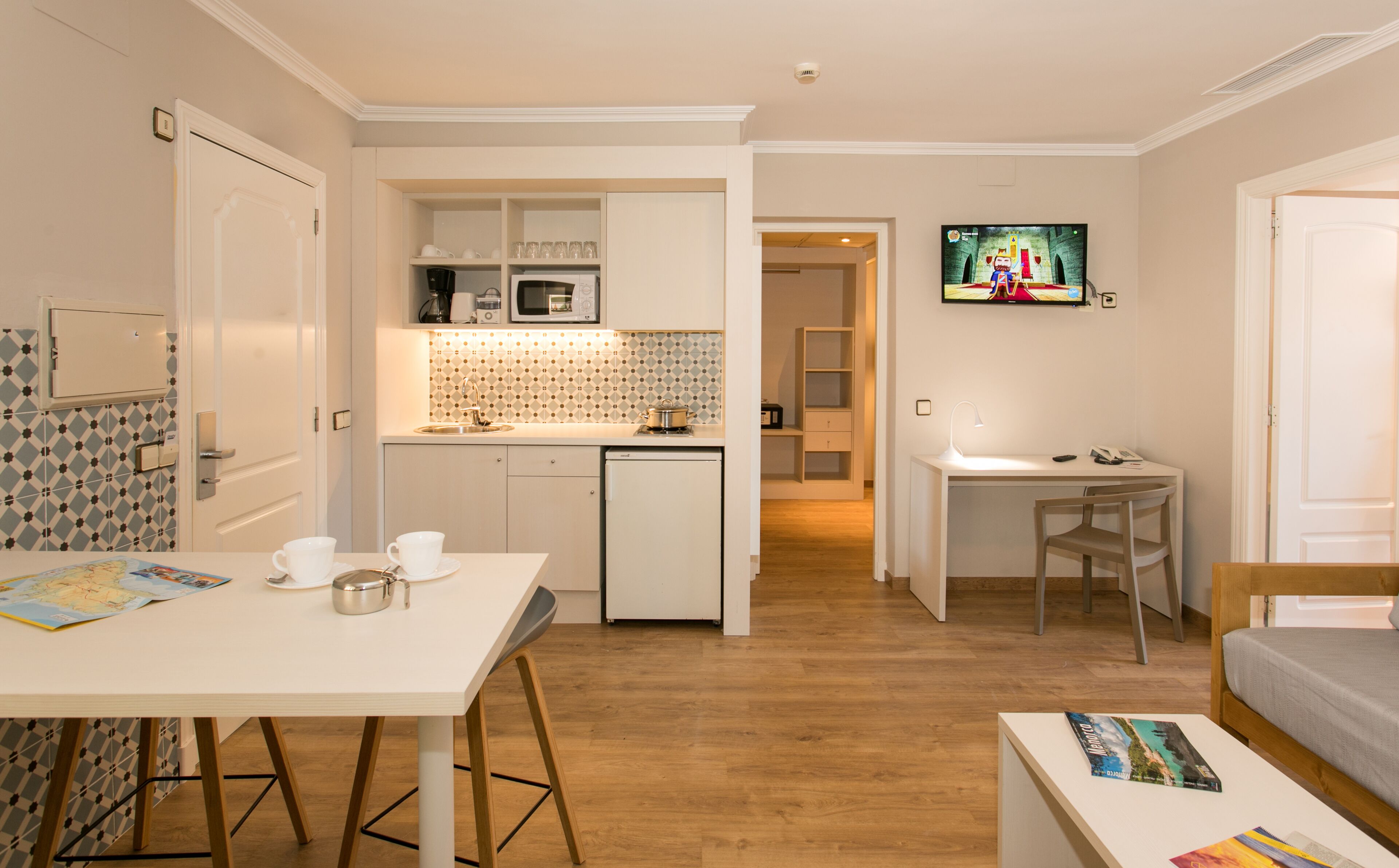 Habitación de hotel compacta con kitchenette, zona de comedor, televisor montado en la pared y una cama.