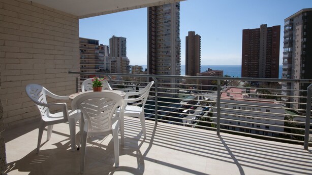 Ein Balkon mit weißen Plastikstühlen und einem Tisch mit einem Blumentopf.