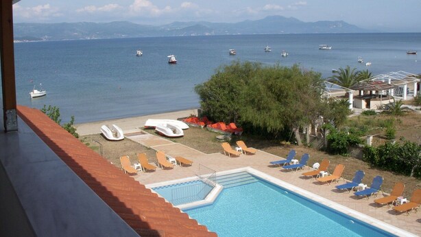 Piscina con sillones de descanso y vista al mar con barcos.