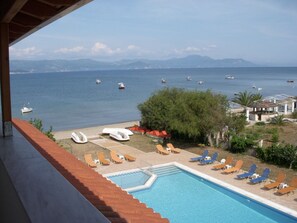 A pool with lounge chairs and a view of the sea with boats. - Likourgos Beach (Corfu)