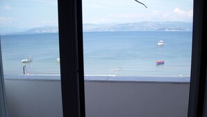 Vista desde un balcón sobre un mar tranquilo con barcos, una costa lejana y montañas.