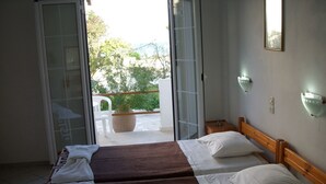 Habitación de hotel con dos camas, un balcón con planta en maceta y vistas al exterior con vegetación.