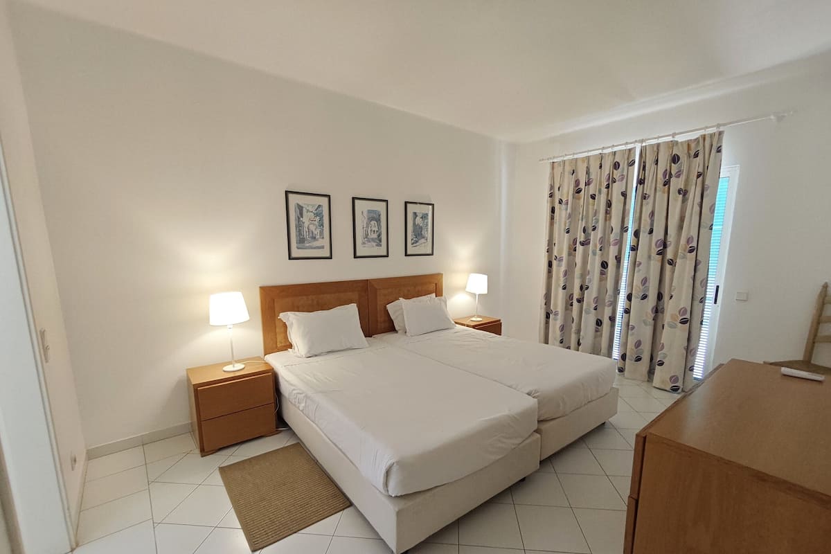 A hotel room with a large bed, two bedside tables with lamps, a wooden headboard, and three framed pictures on the wall.