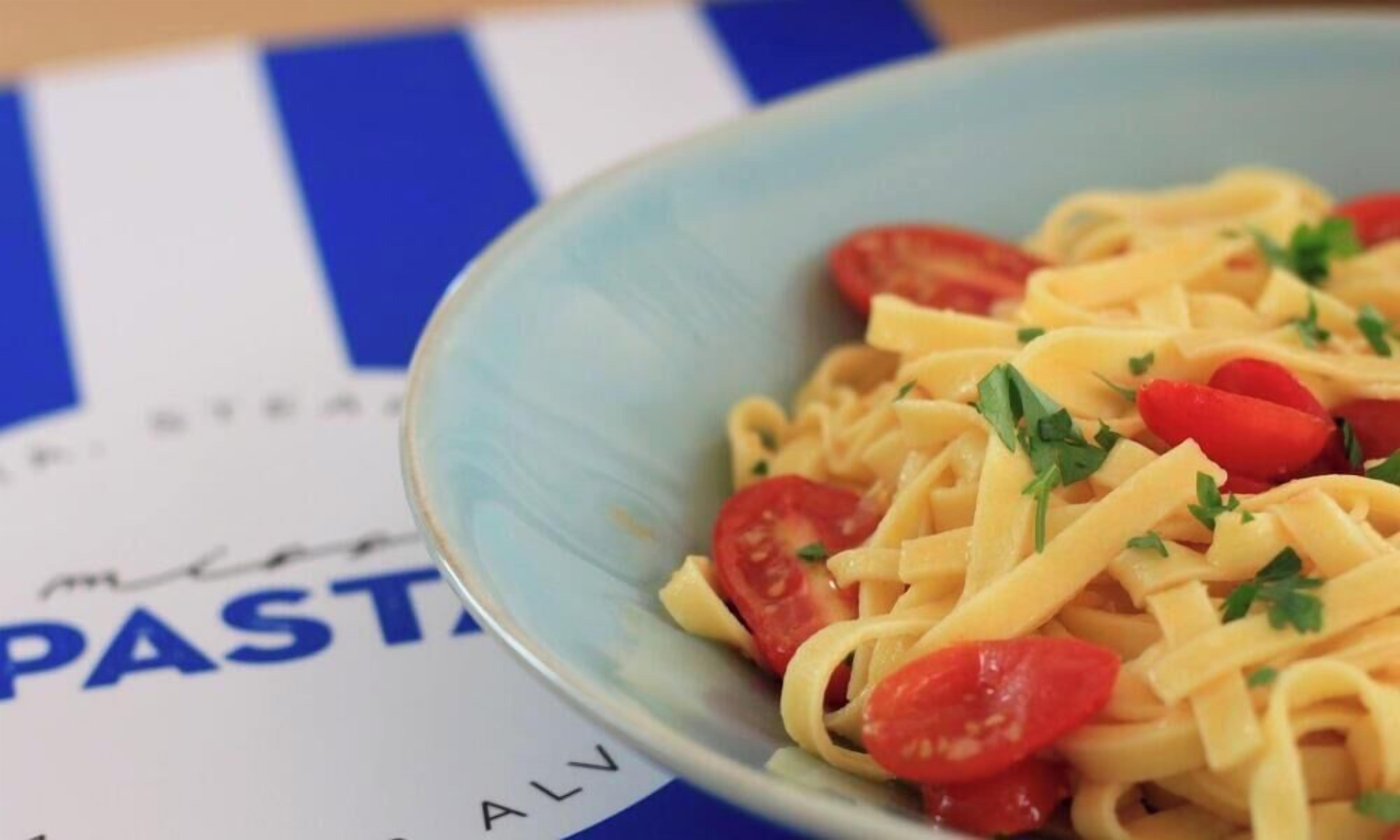 A bowl of pasta with cherry tomatoes and parsley on a table with a blue and white striped napkin.
