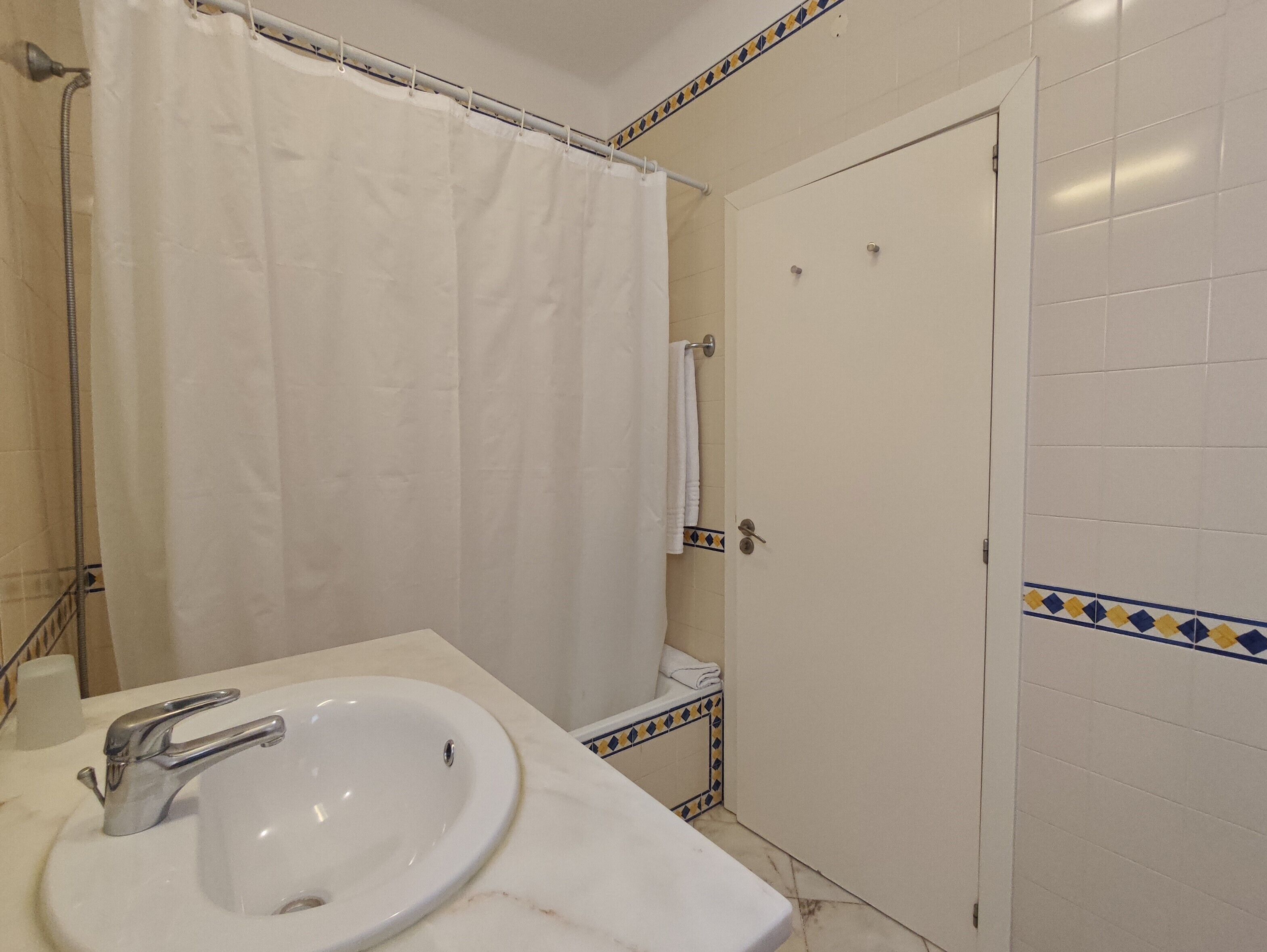 A bathroom with a white sink, a shower curtain, and a door with a towel hanging on it.
