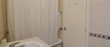 A bathroom with a white sink, a shower curtain, and a door with a towel hanging on it.