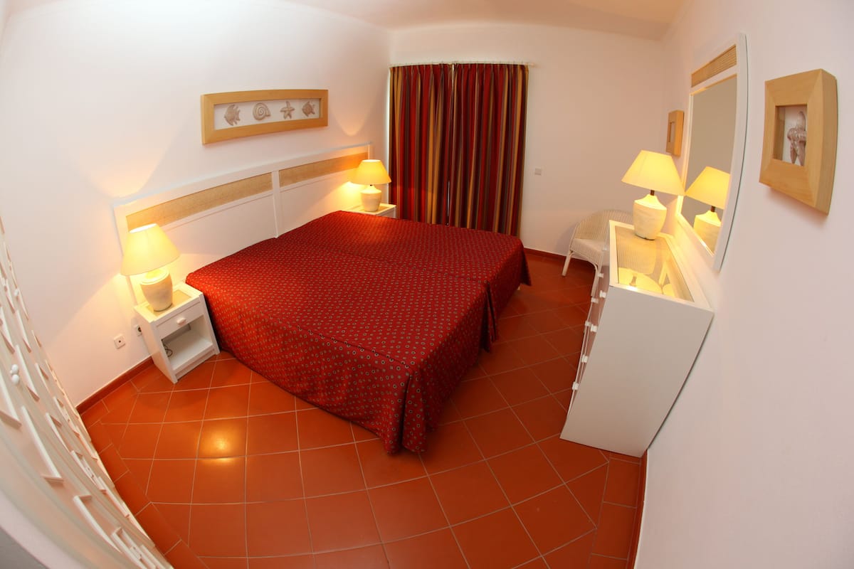 A hotel room with a bed, bedside tables, lamps, a mirror, and a curtain.