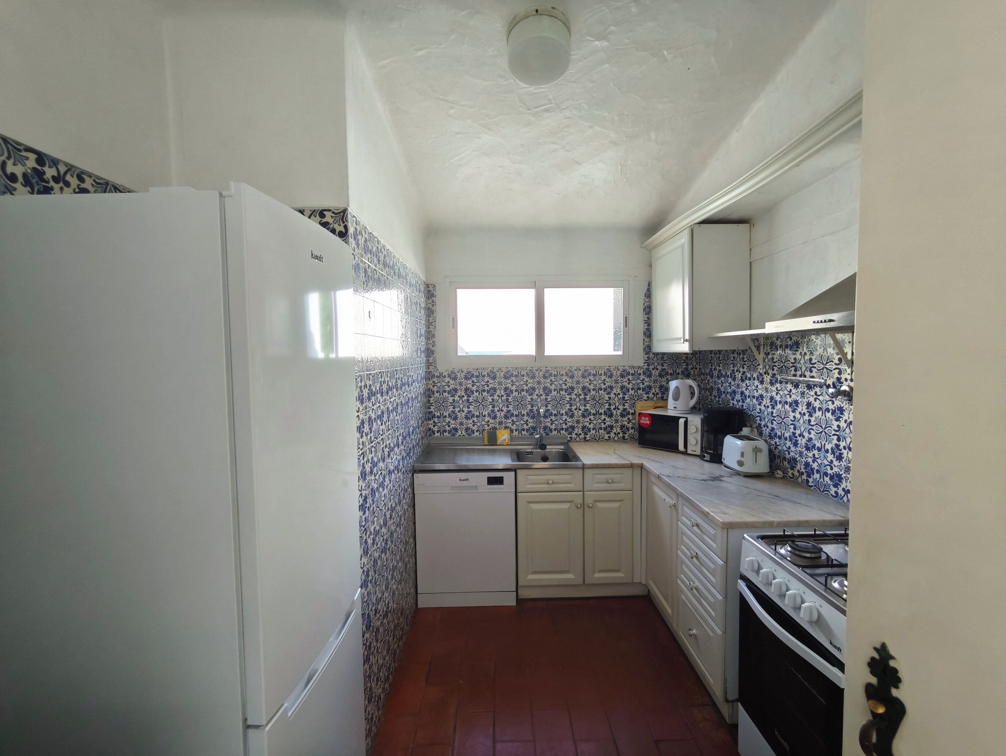 A compact kitchen with white cabinets, a built-in dishwasher, a stove, and a microwave.