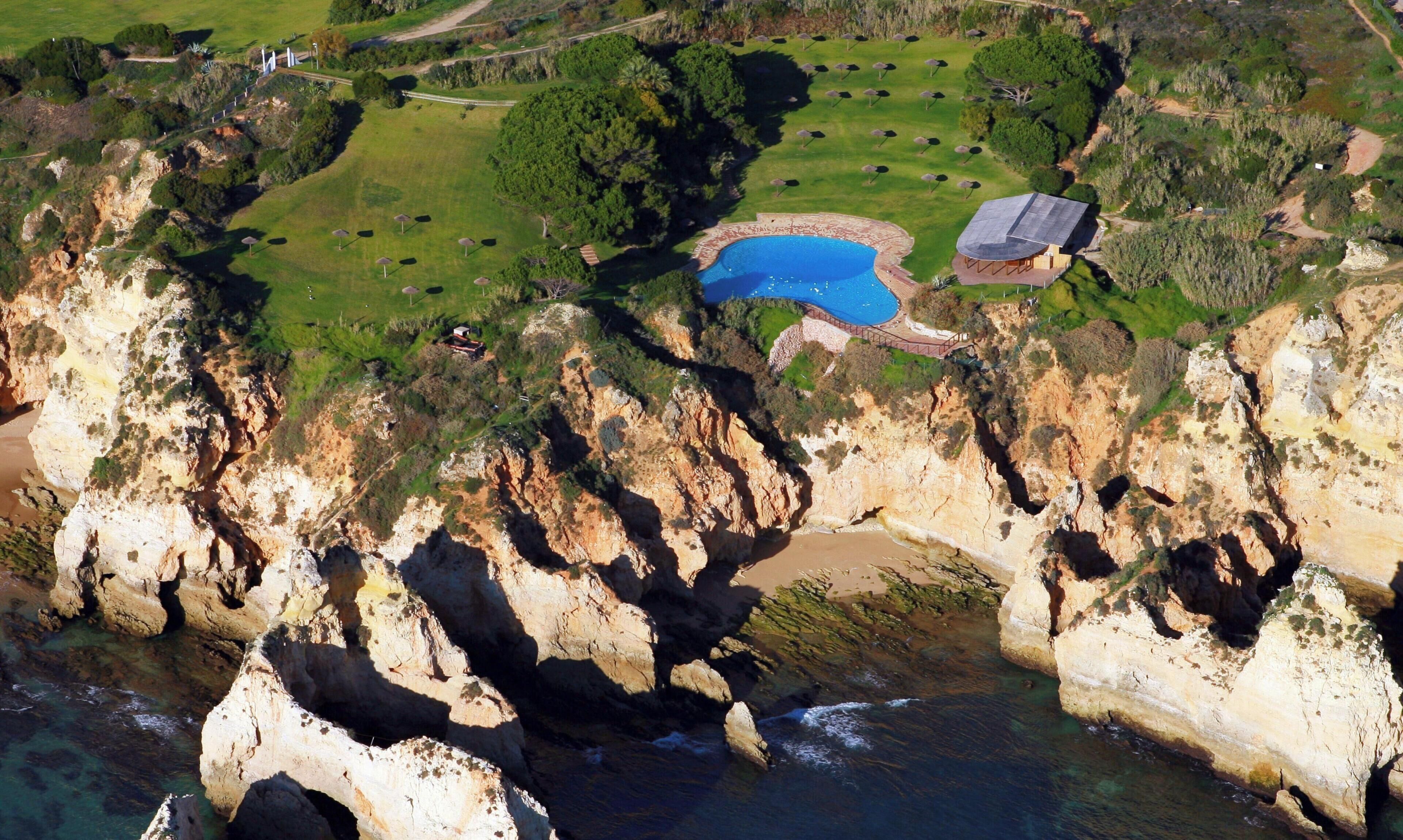 Vista aérea de una propiedad costera con piscina, campo de golf y zona de playa.