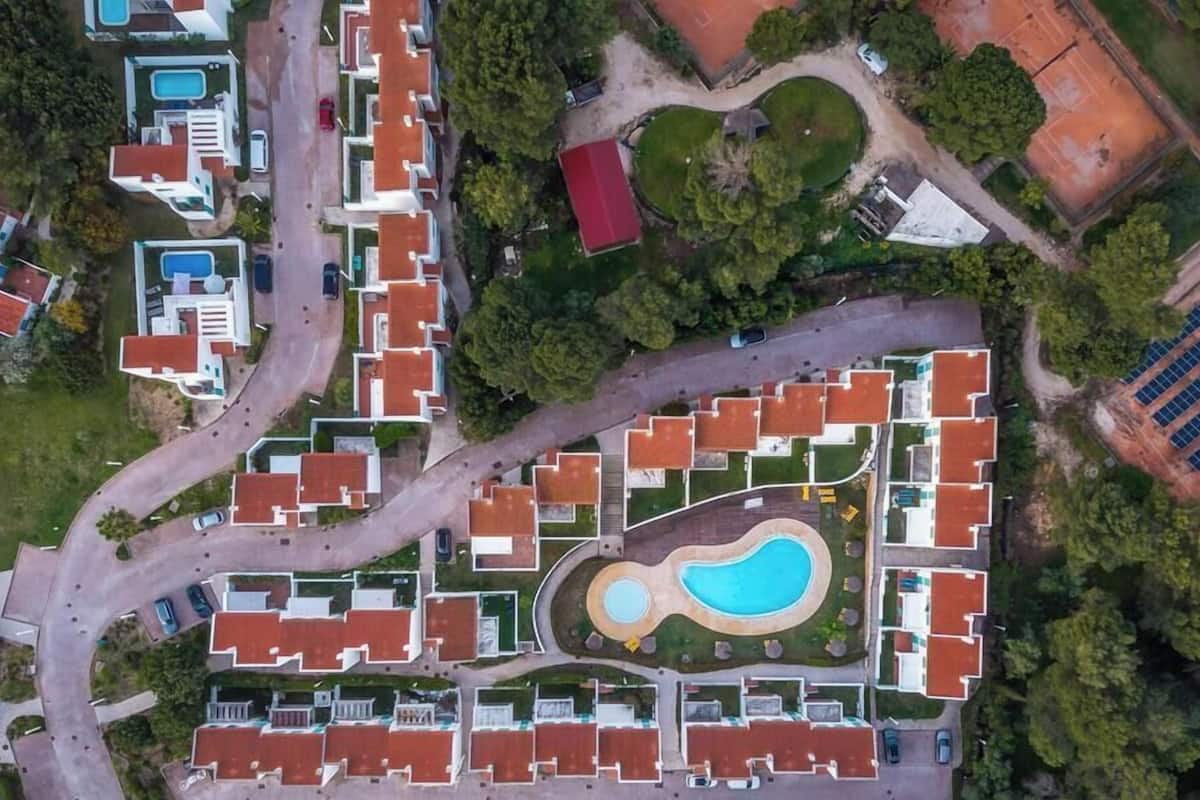 An aerial view of a residential area with multiple buildings, roads, a swimming pool, and solar panels.