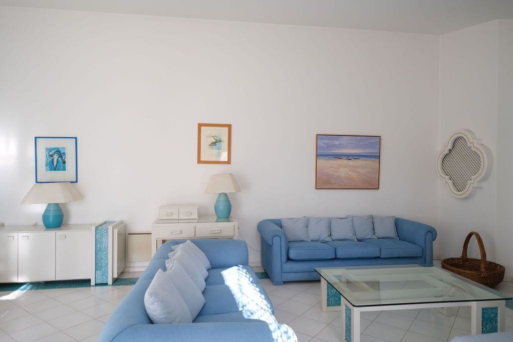 A living room with a blue sofa, a glass coffee table, a white cabinet, and a wall-mounted lamp.