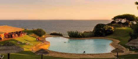 Piscina con vista al mar, rodeada de césped y sillas de descanso.