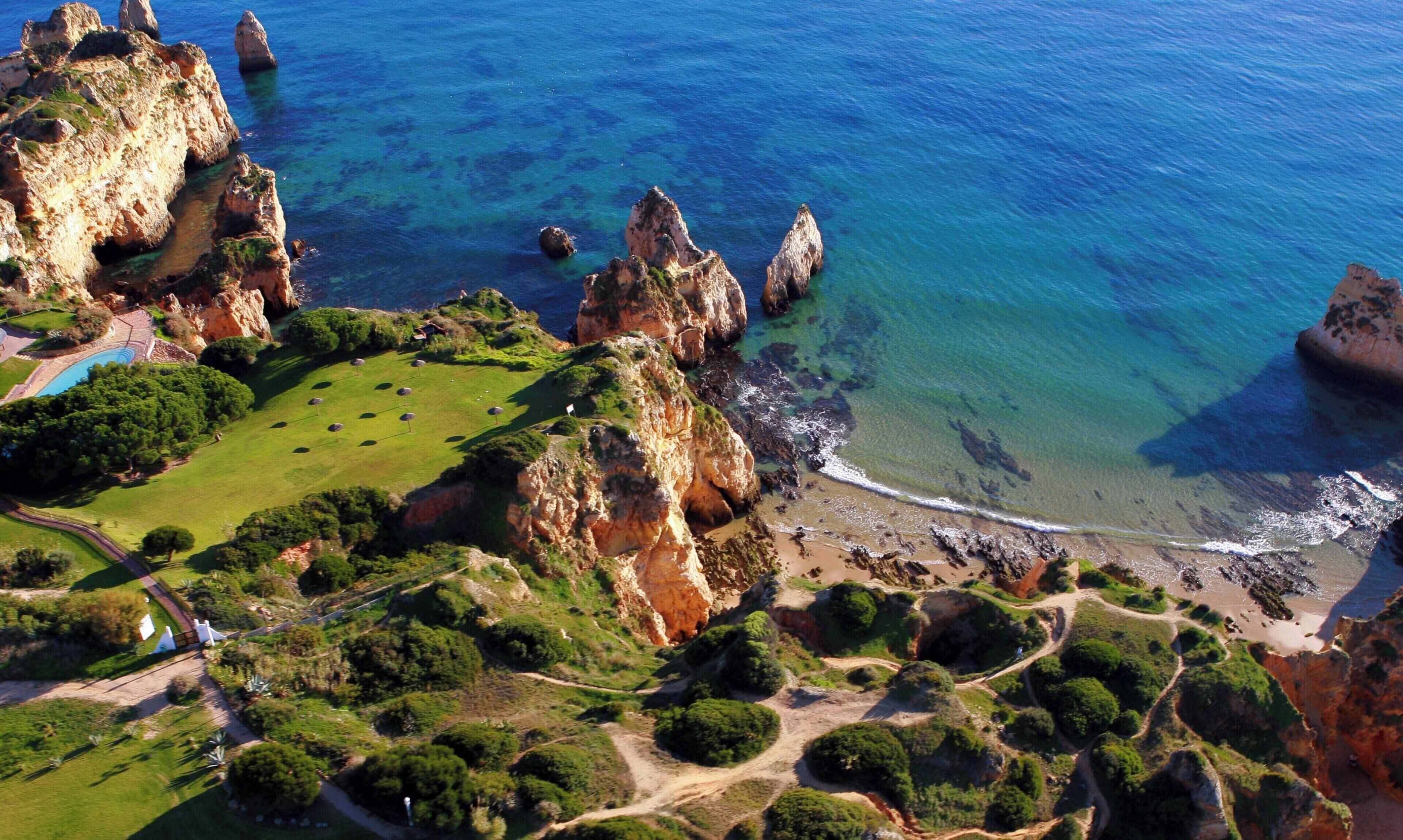 An aerial view of a coastal area with rocky cliffs, a beach, and a golf course.