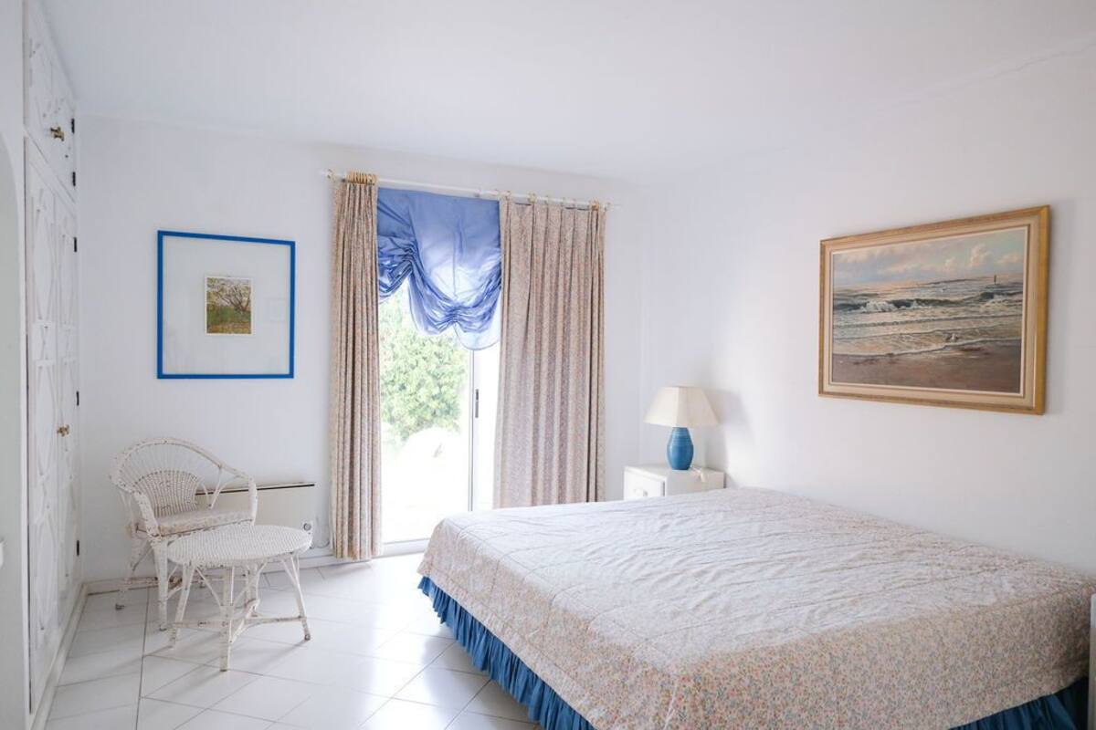 A bedroom with a bed, a chair, a lamp, and a painting on the wall.