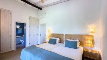A bedroom with a large bed, two bedside tables with lamps, a wooden ceiling fan, and a door leading to a bathroom.