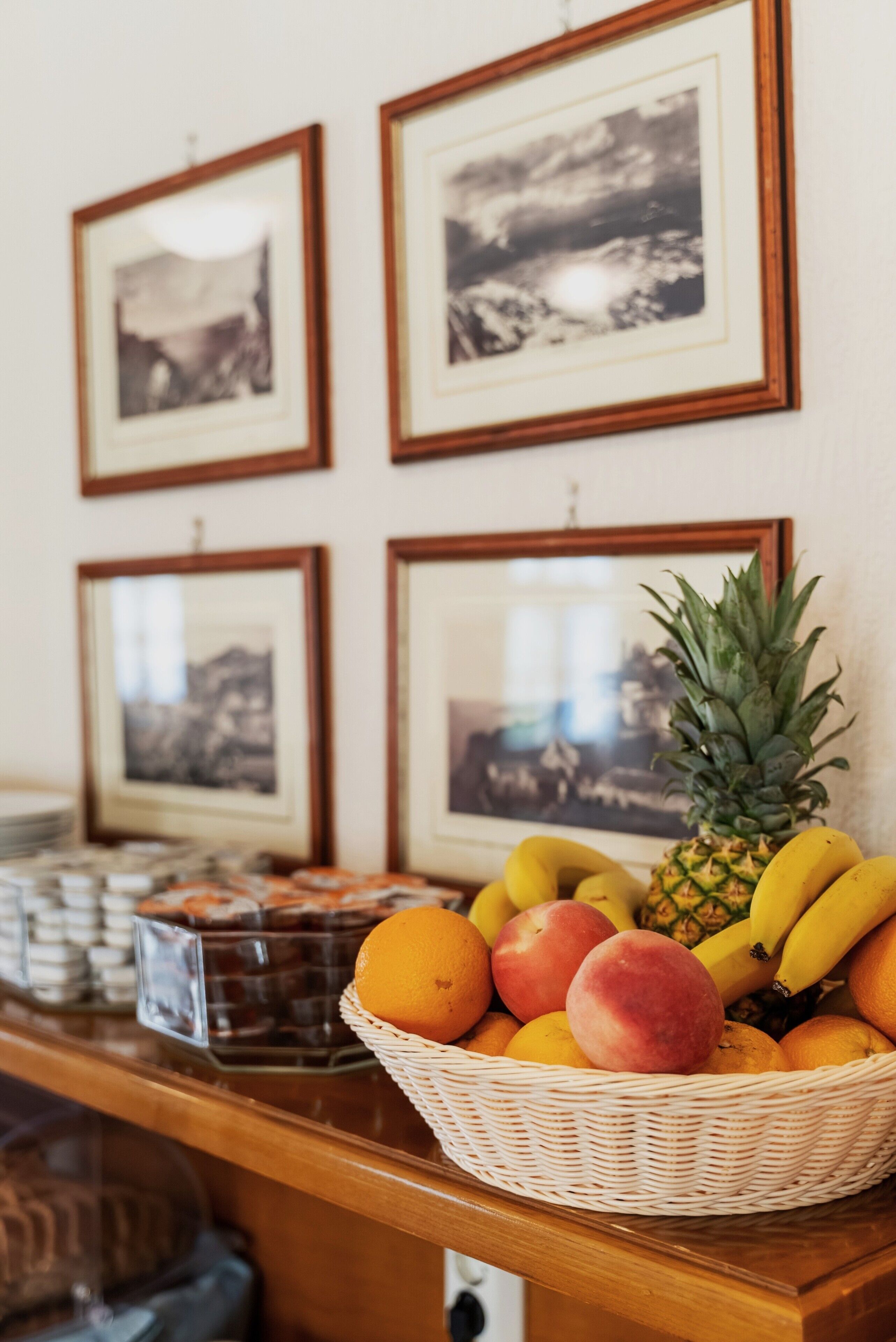A fruit basket on a counter with framed pictures on the wall behind.