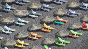 A beach with rows of lounge chairs and thatched umbrellas. - Artemis Hotel (Santorini)