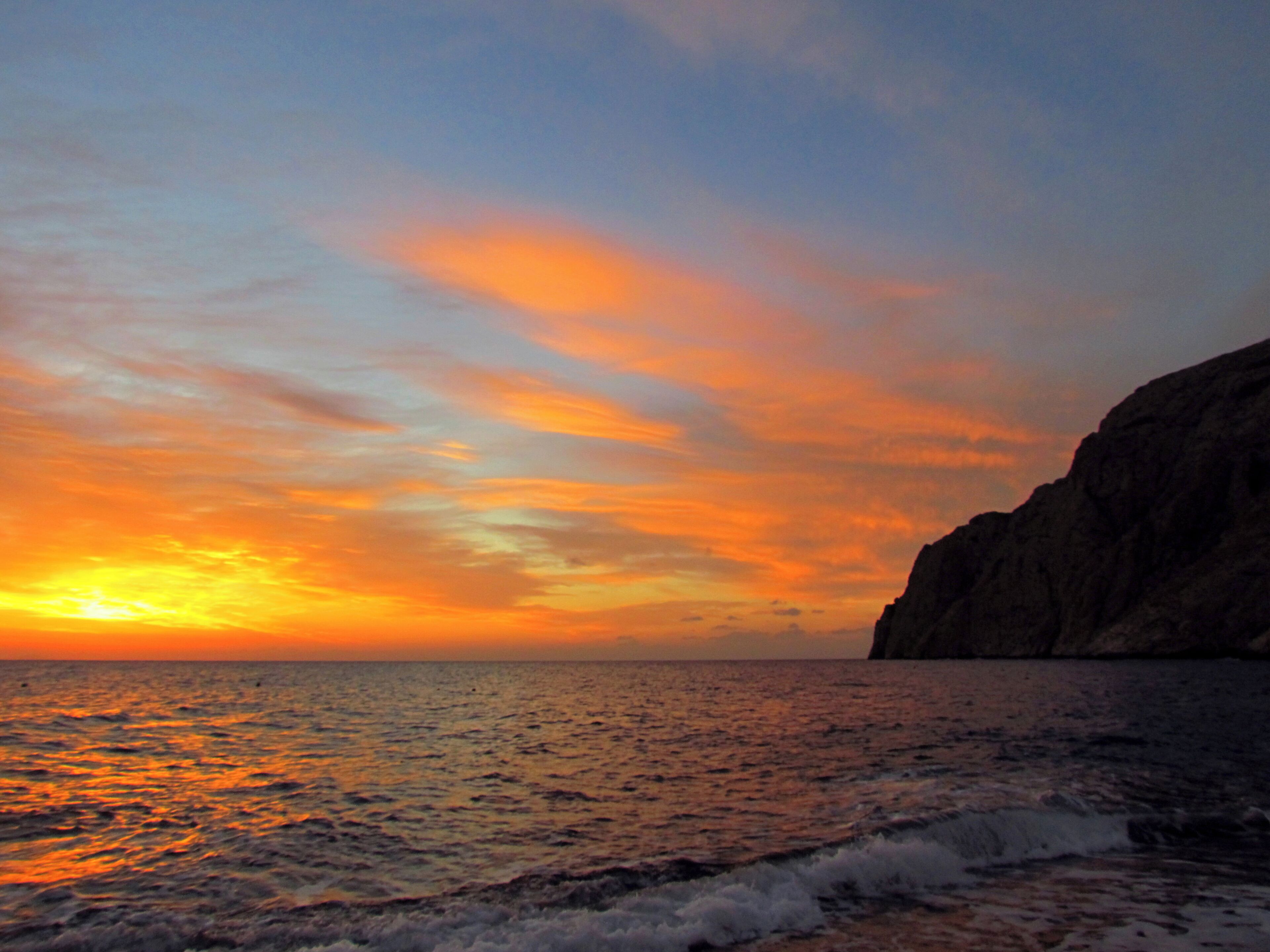 Un atardecer sobre el océano con una costa rocosa.