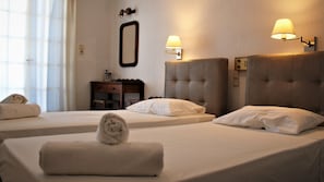 A hotel room with two beds, each with a headboard and a bedside lamp. There is a nightstand with a mirror and a lamp, and a window with curtains. - Artemis Hotel (Santorini)