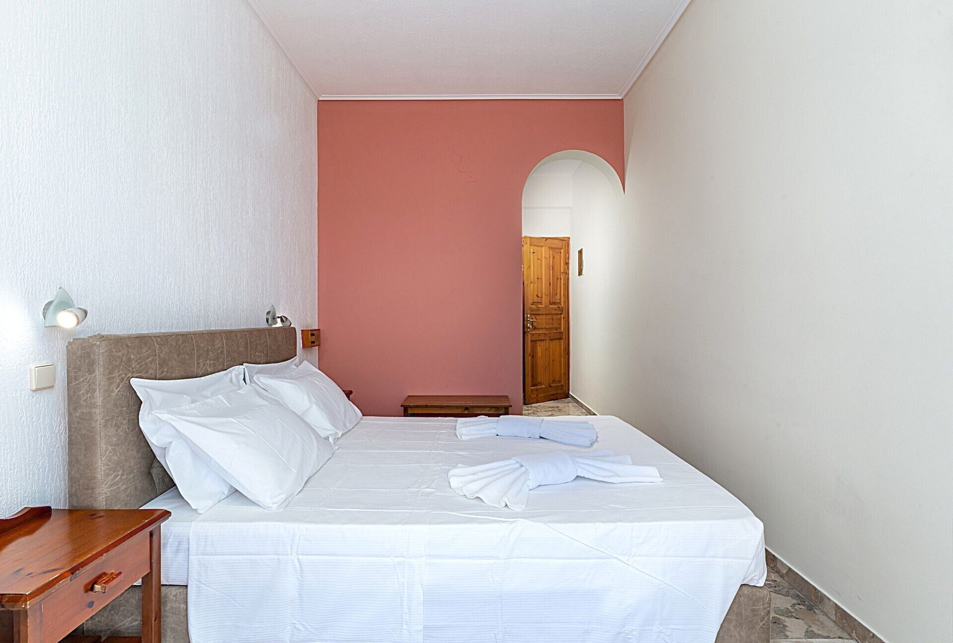 Ein Hotelzimmer mit einem Bett, einem Nachttisch, einer Wandlampe und einer Holztür.