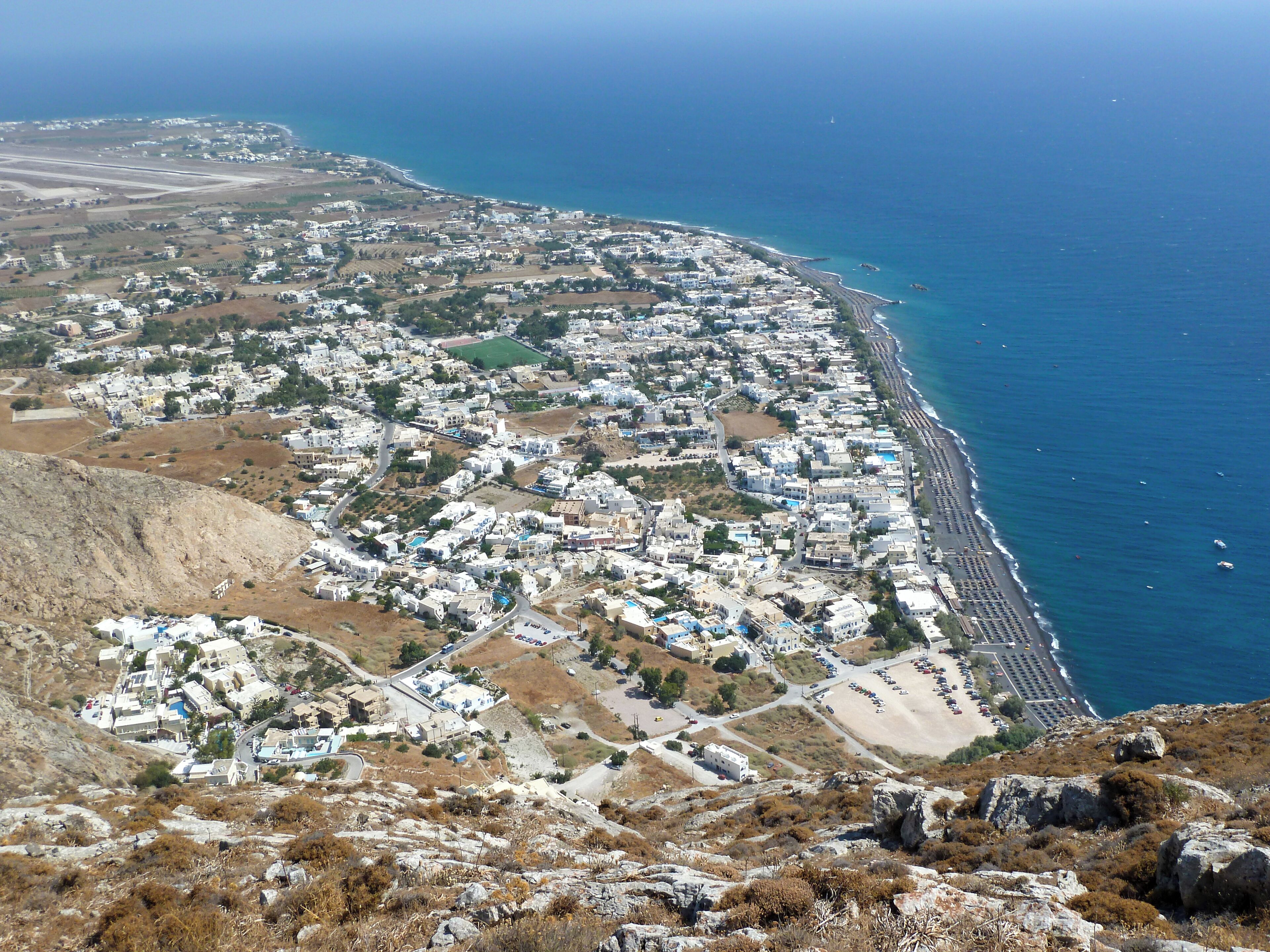 A coastal town with buildings along the beach, a clear view of the sea, and rocky terrain.