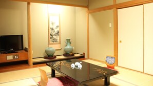 A traditional Japanese room with tatami flooring, a low table, a television, and a sliding door. - Fujisan Isawa Onsen Hotel Sekitei (Fuefuki)