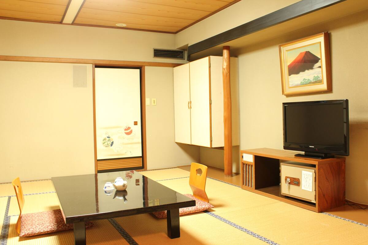Une pièce de style japonais traditionnel, avec un sol recouvert de tatamis, une table basse, un téléviseur et des portes coulissantes.