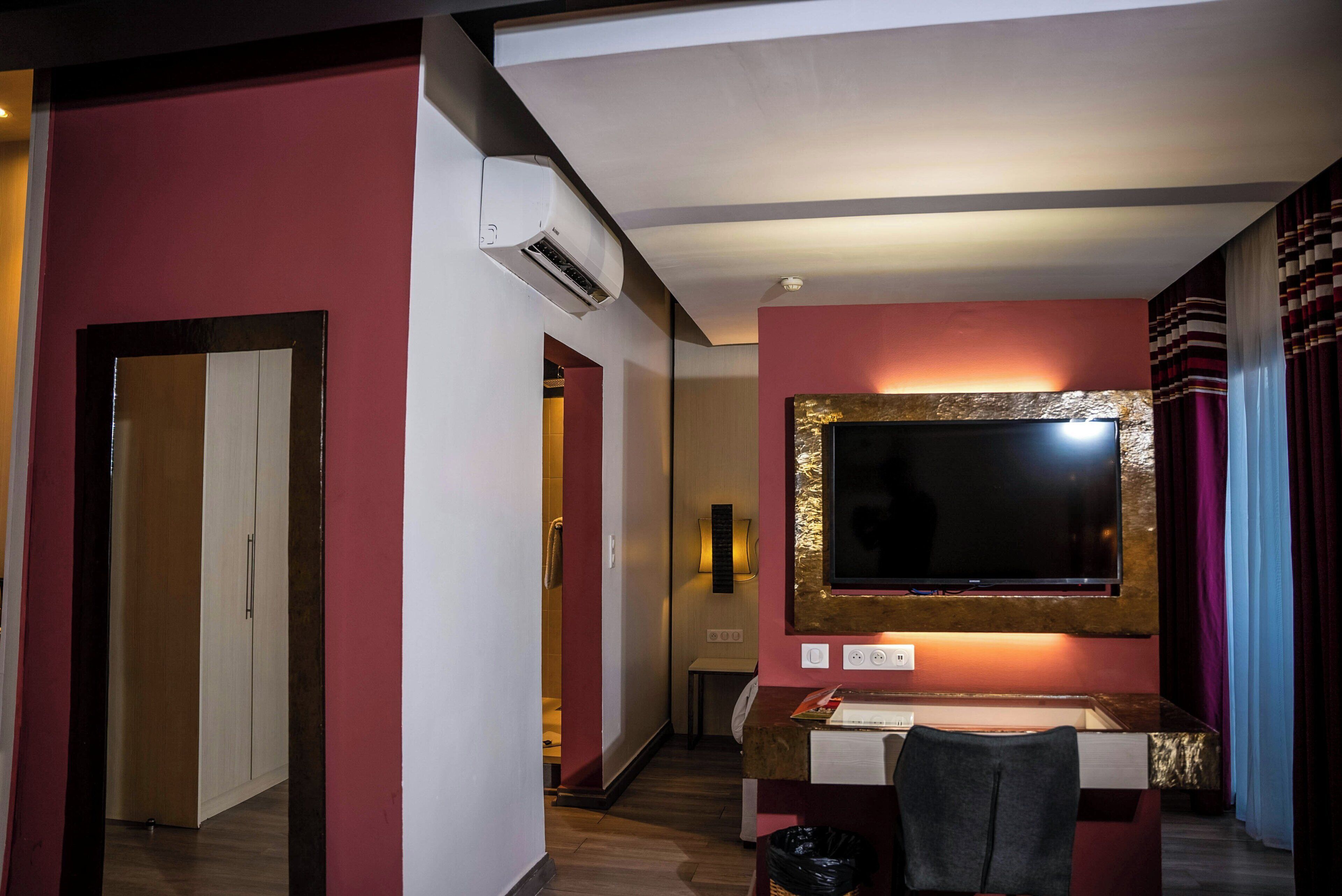 Habitación de hotel con escritorio, televisión montada en la pared, aire acondicionado y puerta que da a otra habitación.
