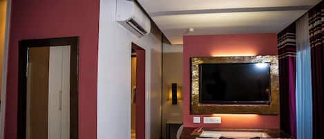 Habitación de hotel con escritorio, televisión montada en la pared, aire acondicionado y puerta que da a otra habitación.
