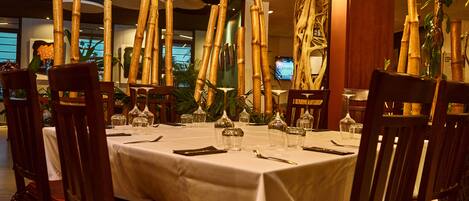 Restaurante com toalha de mesa branca, cadeiras de madeira e decorações de bambu.